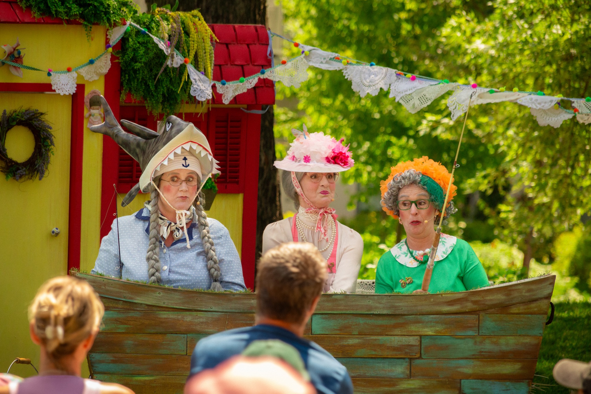 3 people dressed as senior women, doing a play on a stage in a park