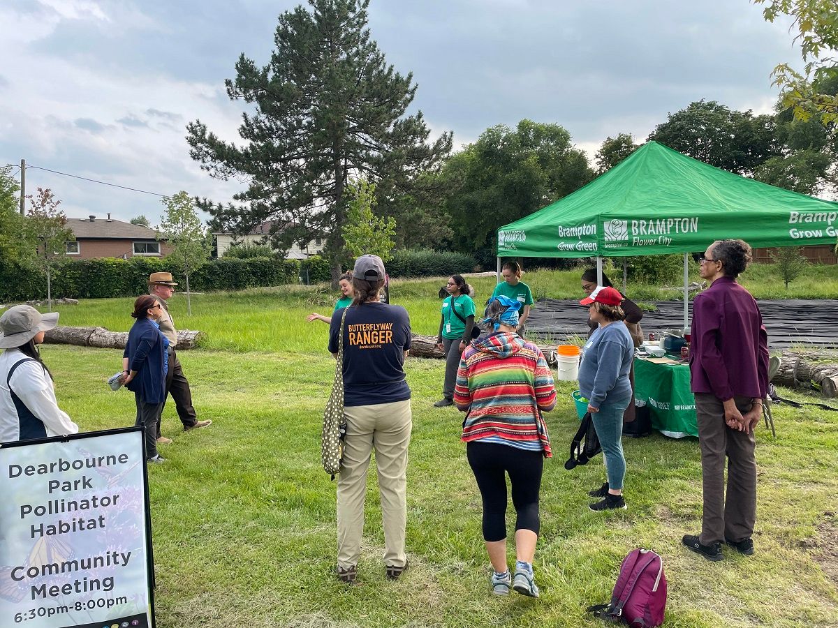 People coming together in a park with a Pollinator habitat sign