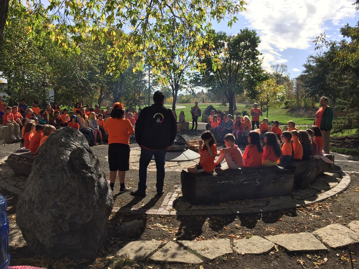 Un grand groupe d'enfants rassemblés autour d'un feu sacré, portant un t-shirt orange.