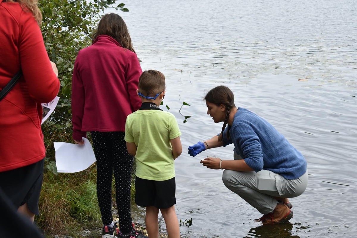 Des enfants écoutant un guide environnemental près d’un lac.