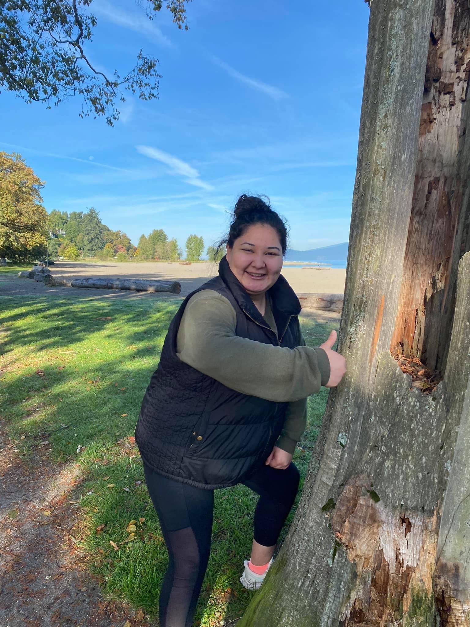 Person doing a thumbs up next to a tree